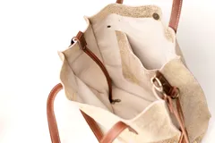 Bolso tipo tote de cuero con acabado texturizado en tono blanco desgastado. Cuenta con doble asa de mano y una correa larga ajustable y extraíble en color tostado. Presenta un bolsillo frontal externo y herrajes metálicos.