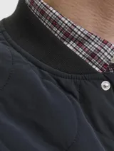 Campera acolchada color negro con diseño de costuras onduladas, cuello estilo baseball y cierre frontal con botones a presión. Presenta un bolsillo tipo parche en el pecho con etiqueta de marca y dos bolsillos laterales inferiores.