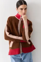 Campera de lana con cuello alto y cierre frontal de doble cursor. Presenta un diseño de bloques de color en tonos marrón, rosa y rojo, con detalles de tejido trenzado en las mangas y bolsillos laterales.