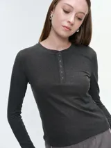 Remera de manga larga confeccionada en tejido acanalado, con escote redondo y cierre frontal con botones. Presenta un ajuste entallado al cuerpo.