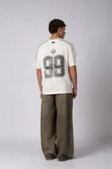 Remera de algodón color blanco con corte regular, cuello redondo y mangas cortas. Presenta detalles de líneas finas negras en los hombros y estampado gráfico frontal con tipografía y logotipos en color negro.