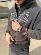 Campera canguro con cierre frontal, capucha y bolsillos tipo canguro, en tono marrón con efecto gastado vintage y estampa gráfica blanca con detalles de strass en el pecho.