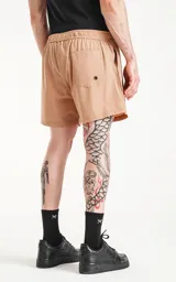 Short de baño color beige con cintura elástica y cordón ajustable. Cuenta con tres bolsillos y un parche con logo en la pierna izquierda.