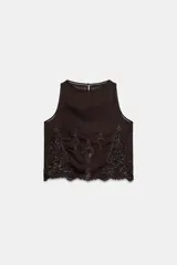 Top marrón oscuro de cuello redondo y manga sisa, con detalles de bordados y entredoses geométricos y florales a tono. Cuenta con abertura y cierre de botón en la espalda.