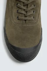 Zapatilla de cordones color verde militar, con parte superior de piel con acabado serraje y detalle de pespuntes en el empeine. Tiene horma redonda y suela plana de goma en color negro.