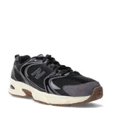 Championes New Balance modelo 530, con diseño retro-deportivo. Presentan una capellada de malla transpirable en color negro con refuerzos sintéticos en tonos grises y negros. Incluyen entresuela con tecnología ABZORB en color crema y suela de goma en tono marrón.