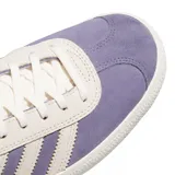 Championes Adidas modelo Gazelle ADV, confeccionados en gamuza color lavanda con las icónicas tres tiras y detalles en color crema. Presentan el nombre del modelo en letras doradas en el lateral y una suela de goma texturizada.