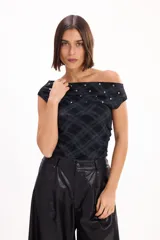 Top negro con estampado tartán, escote off-shoulder, mangas cortas y detalle de tachas plateadas en el escote.