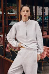 Pantalón jogger de felpa color gris claro melange, de tiro medio con cintura elástica. Presenta detalles de aplicaciones tejidas a contraste en los laterales y terminaciones con puños abullonados.