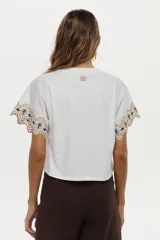 Blusa blanca de jersey con mangas cortas amplias de tela plana, decoradas con bordados geométricos en tonos marrón y azul marino.