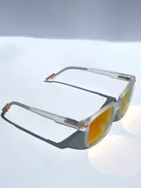 Lentes de sol con armazón de acetato traslúcido en acabado mate y cristales polarizados con efecto espejado en tono naranja. Presentan detalles en color naranja en las patillas y el frente.