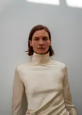 Camisa de cuello alto y manga larga, confeccionada en tejido satinado de acabado suave. Presenta un diseño recto y cierre de cremallera en la parte posterior.