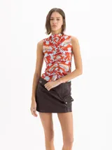 Top al cuerpo sin mangas con escote alto tipo polera y detalle de frunce en el centro delantero. Presenta un estampado full print de flores hibiscos en tonos rojos y naranjas sobre base celeste.