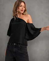Blusa satinada negra de un solo hombro, con mangas amplias y caída fluida.