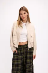 Campera corta de cuero sintético en color beige, con diseño de calce relajado, cierre frontal metálico, bolsillos con solapa en el frente y cordón ajustable en el ruedo.