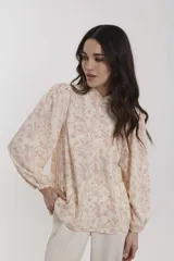 Blusa color crema con estampado floral en tonos rosados, cuello mao con botones y mangas largas abullonadas con puños elásticos.
