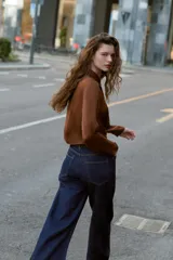 Camisa corta de manga larga, color crema o beige muy claro, con cuello solapa y escote drapeado o fluido tipo cascada.