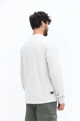 Remera de manga larga color blanco roto o gris muy claro, con escote redondo y un pequeño logo circular estampado en el pecho.