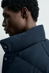 Campera puffer acolchada de corte regular fit, confeccionada en tejido técnico azul marino repelente al agua. Relleno interior de 80% plumón y 20% pluma. Cuenta con cuello subido, manga larga con puño elástico, bolsillos frontales de plastrón con solapa y cierre de cremallera oculta con solapa de botones a presión.