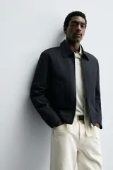 Cazadora cropped fit color azul marino, confeccionada en tejido de algodón. Presenta cuello solapa, manga larga con puño abotonado, bolsillos frontales de vivo y un bolsillo interior. El cierre es frontal con cremallera.