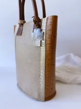 Bolso matero de cuero color beige con textura de reptil y detalles en cuero marrón con textura de cocodrilo. Incluye manijas cortas de cuero marrón y dije de cruz plateada.