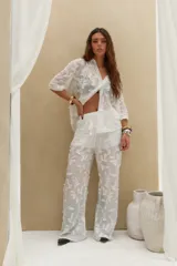 Pantalón largo blanco de corte recto y holgado, confeccionado en tejido semitransparente con diseño bordado de motivos vegetales. Cuenta con cintura elástica ajustable con cordón.