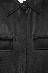 Camisa sin mangas de tejido satinado, con cuello solapa, cierre frontal con botones ocultos y bolsillos de plastrón con solapa en el delantero. Presenta un bajo asimétrico y corte recto.