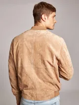 Campera bomber color marrón claro confeccionada en gamuza, con cierre frontal y bolsillos laterales con botón a presión. Presenta cuello, puños y cintura acanalados.