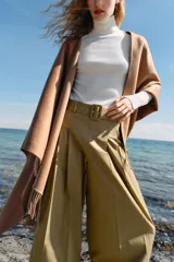 Jersey de punto liso en color beige, con cuello alto y manga larga con detalle de botones metálicos en los puños.