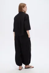 Camisa negra de viscosa, holgada, con mangas cortas abotonadas, cuello camisero, detalles de cintas decorativas verticales y cierre frontal con botones.