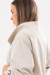 Trench de gabardina Tencel color beige, de silueta relajada, con cierre frontal de botones, lazo desmontable y regulable en la cintura, bolsillos amplios y lazos en los puños.
