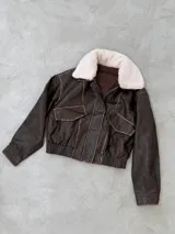 Campera tipo gamulán de cuero gastado color marrón, con cuello de corderito sintético en color crema, cierre frontal y cintura elástica.