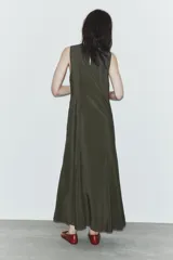 Vestido midi de tejido fluido en color verde oscuro, con cuello redondo y diseño sin mangas. Presenta un corte entallado en el torso que se abre en una falda evasé con pliegues en el bajo. Incluye cierre lateral con cremallera oculta y abertura con botón en la espalda.