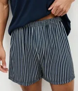 Pijama corto masculino confeccionado en mezcla de algodón, viscosa y elastano. Incluye una remera de manga corta, cuello redondo y bolsillo frontal con detalle listrado, combinada con un short de rayas finas y cintura elástica.