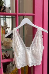 Top de encaje blanco con escote en V profundo, diseño longline y detalles de bordes festoneados.