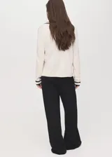 Cardigan de punto fino color blanco crudo, con diseño recto, escote en V, cierre frontal con botones y rayas negras en contraste en la tapeta y los puños.