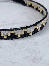 Pulsera tejida a mano con cuentas Miyuki cilíndricas en patrones alternados de negro, dorado y blanco translúcido.