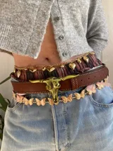 Cinturón marrón de cuero sintético con hebilla dorada en forma de cráneo de toro.