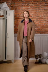 Trench larga de estilo encerado en color marrón, con cuello de pana en contraste y cierre frontal con botones a presión.