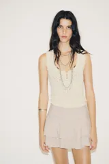 Falda pantalón corta color beige claro, de tiro medio, con efecto drapeado en la cintura y volantes superpuestos en el ruedo.