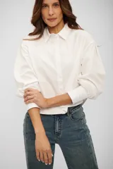 Camisa de corte cropped y diseño holgado, color blanco, con cuello clásico, cierre frontal de botones y mangas largas con puños anchos.