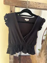 Top negro de textura gofrada, con escote en V cruzado, mangas cortas con volados y cintura fruncida con cordón ajustable.
