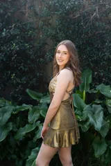 Vestido corto negro con estampado de plumas doradas, escote en V, breteles finos cruzados en la espalda, cut-outs laterales y volado en el ruedo.