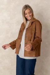 Chaqueta de gamuza sintética color marrón, con diseño de flecos en el pecho y la espalda. Presenta cierre frontal con botones, cuello camisero y bolsillos cuadrados frontales.
