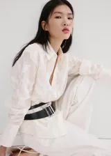 Blusa de diseño recto color crudo con diseño bordado floral, cuello camisero, manga larga con puños anchos abotonados y cierre delantero con botones.