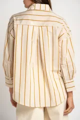 Camisa de corte oversize con estampado de rayas verticales en tonos verde, blanco y ocre. Presenta cuello clásico, cierre frontal con botones, bolsillo en el pecho y mangas largas con puños abotonados.