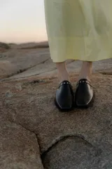 Mules de cuero negro con punta cuadrada y detalle de tachas metálicas en el borde superior.