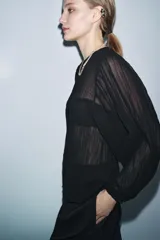 Blusa negra de manga larga abullonada, con tejido plisado y cuello redondo con abertura y botón en la espalda.