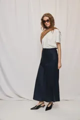Falda larga de color negro, calce al cuerpo y caída fluida, confeccionada en tejido satinado con detalle de recorte diagonal en la parte delantera y cintura elástica.