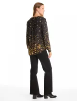 Blusa de gasa con estampado abstracto en tonos amarillos sobre fondo negro. Presenta cuello mao con escote en V y cierre frontal parcial con botones. Las mangas son largas y cuentan con presillas para ajustar su largo.